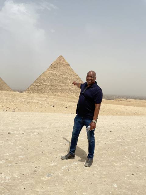 Person pointing towards a pyramid in a desert setting.