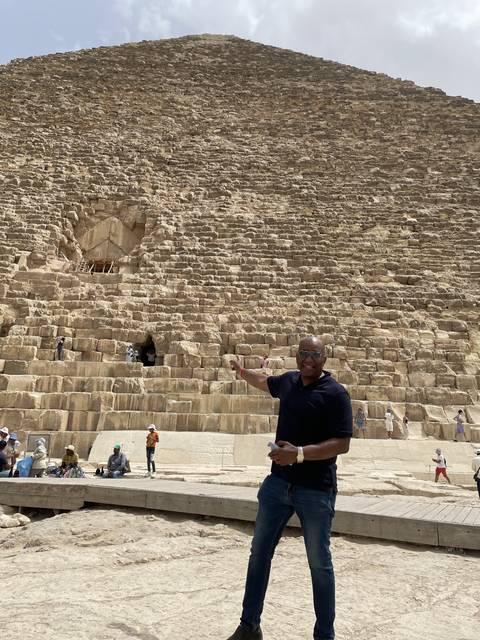       Person pointing towards a pyramid in the desert.
  