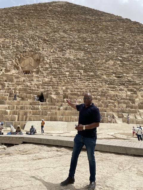       A person standing in front of a large stone pyramid, likely in an Egyptian setting.
  