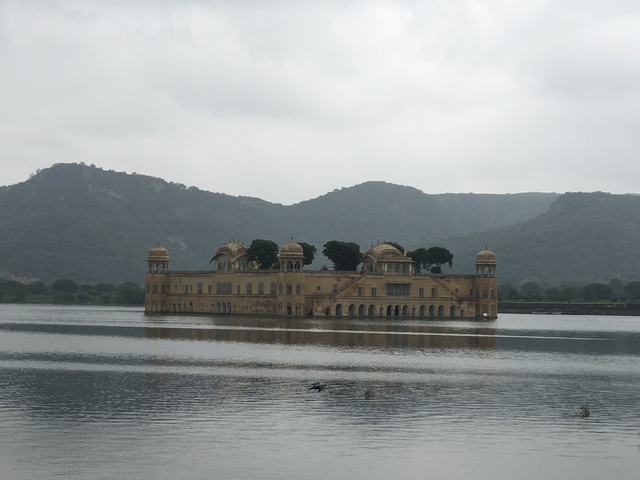 Palatial structure standing on a lake with mountains in the background.