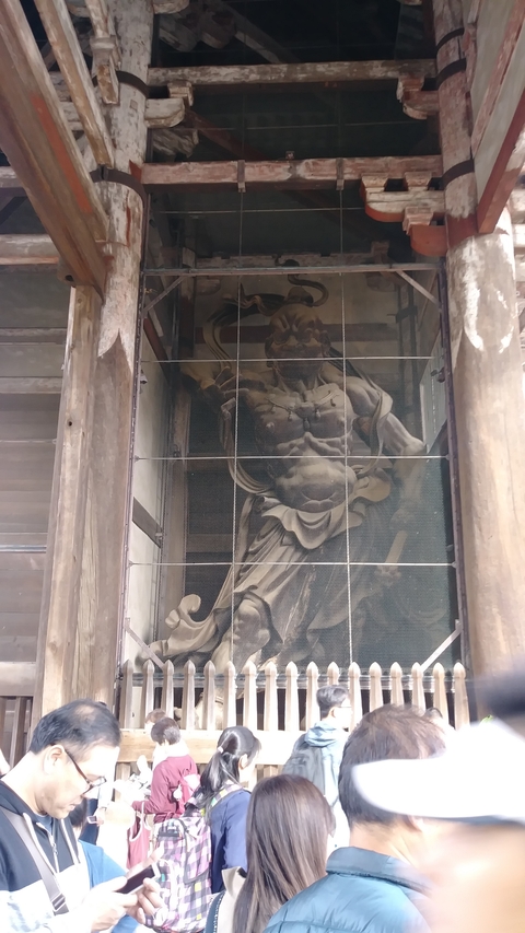       Wooden guardian statue behind a mesh screen.
  