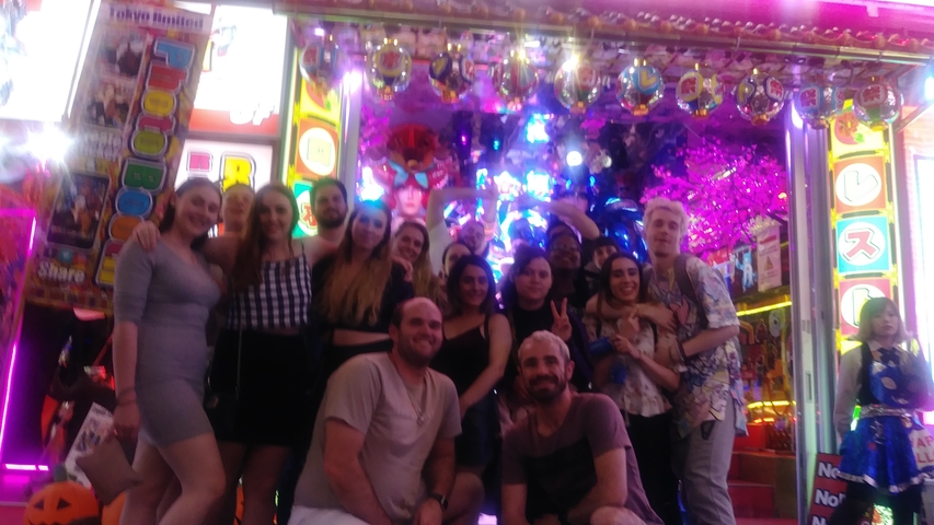       Group of people posing in front of a brightly lit storefront.
  