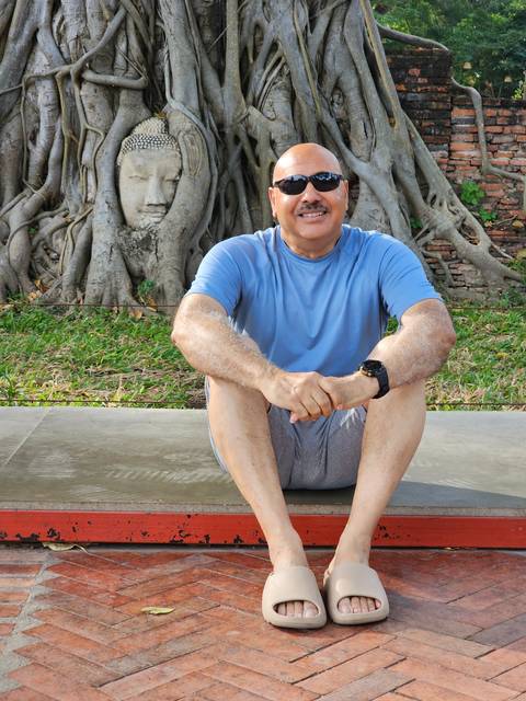 Person sitting in front of a Buddha head entwined in tree roots.