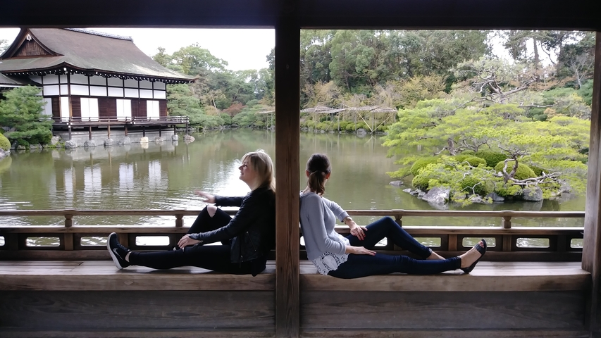       Two women seated back-to-back in a wooden pavilion overlooking a pond.
  