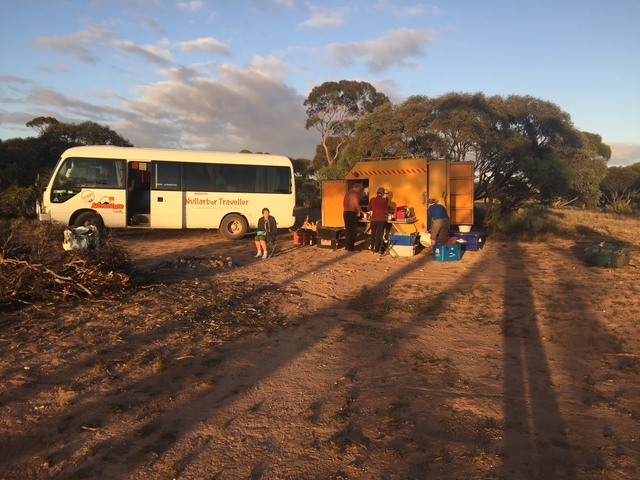       People setting up campsite with a bus parked nearby.
  