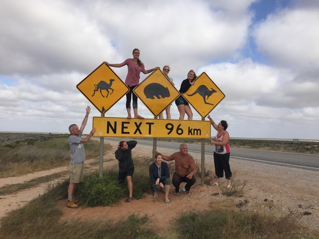       People posing with animal crossing signs next to a road.
  