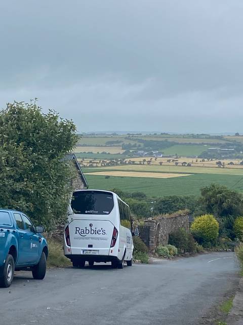 Tour van parked on a roadside with fields in the background.