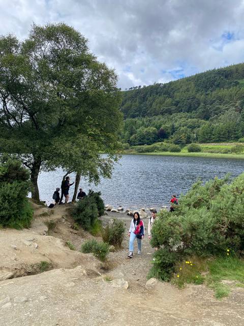 People walking on a path near a lake surrounded by trees.