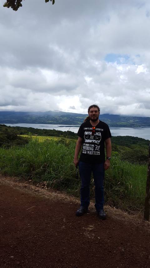       A man standing in front of a scenic landscape with a lake and mountains.
  