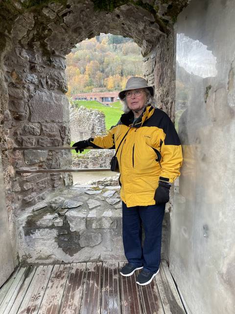       Person standing in a stone archway with autumn scenery outside.
  
