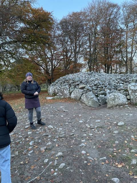      Person standing near ancient stone structures with trees around.
  