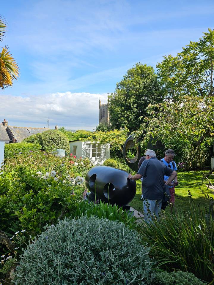 Two people standing in a garden with greenery and a sculpture.