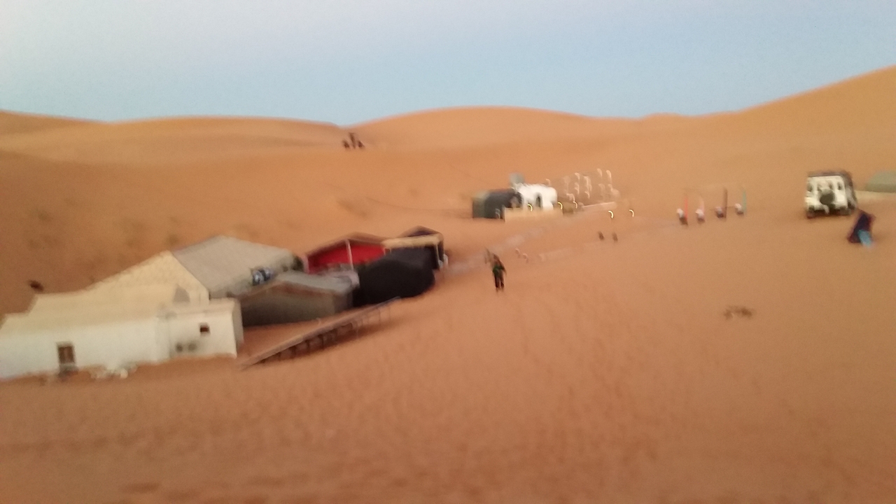 Blurred image of desert camp with tents and vehicles.