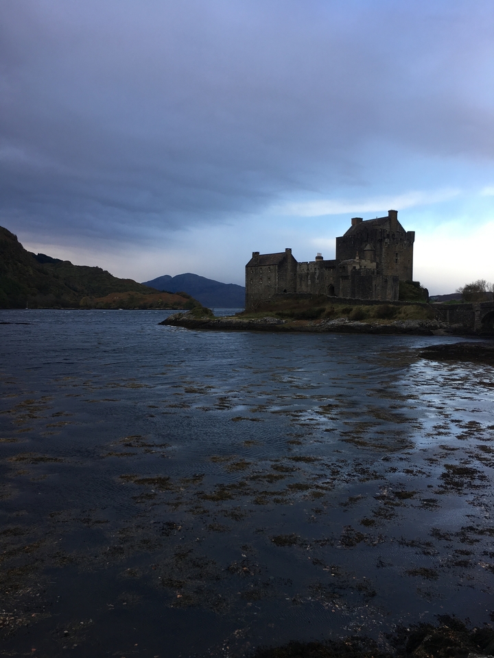 A scenic view of a historic castle with a body of water in the foreground.