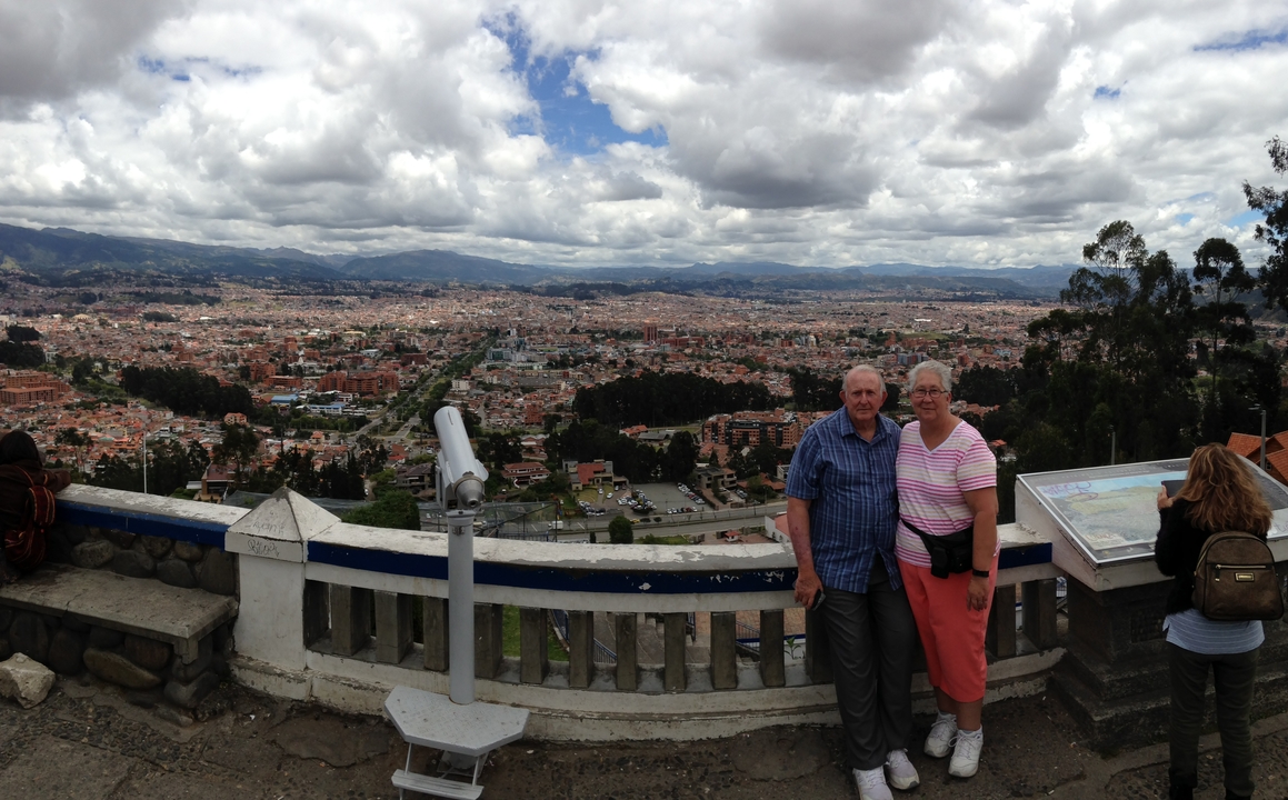 Two older adults posing at a viewpoint overlooking a large city.
