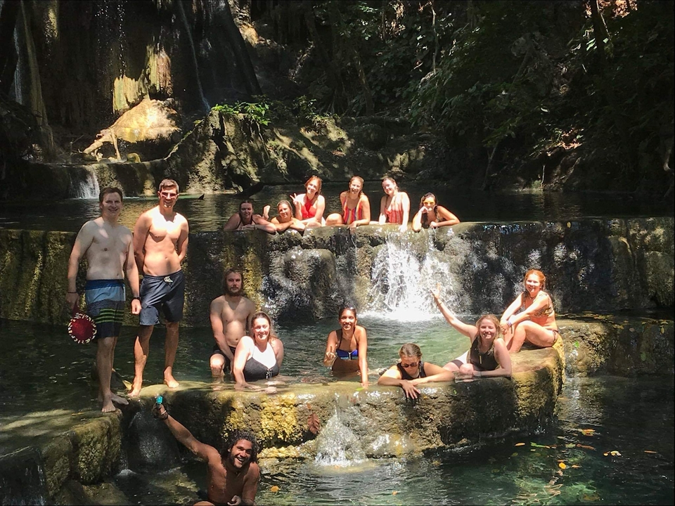 Group of people swimming in a natural waterfall pool.