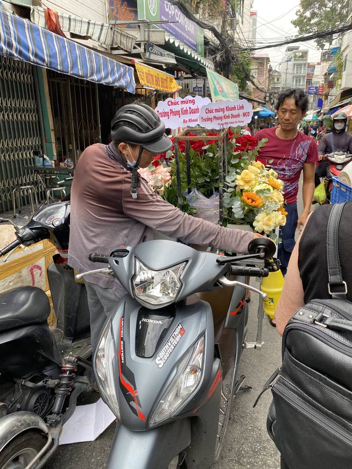 Man on a scooter carrying flowers in a bustling market.