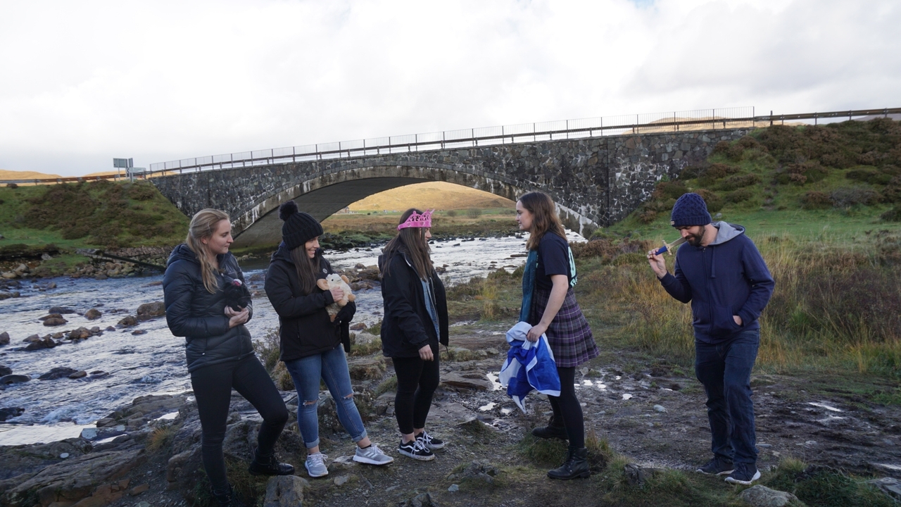 Group of people standing on rocky riverside with a stone bridge in the background
