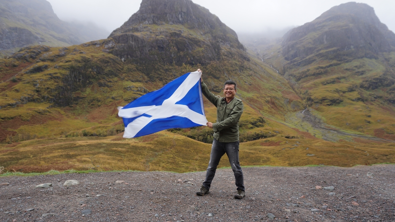 Man holding a Scottish flag in a dramatic mountainous landscape
