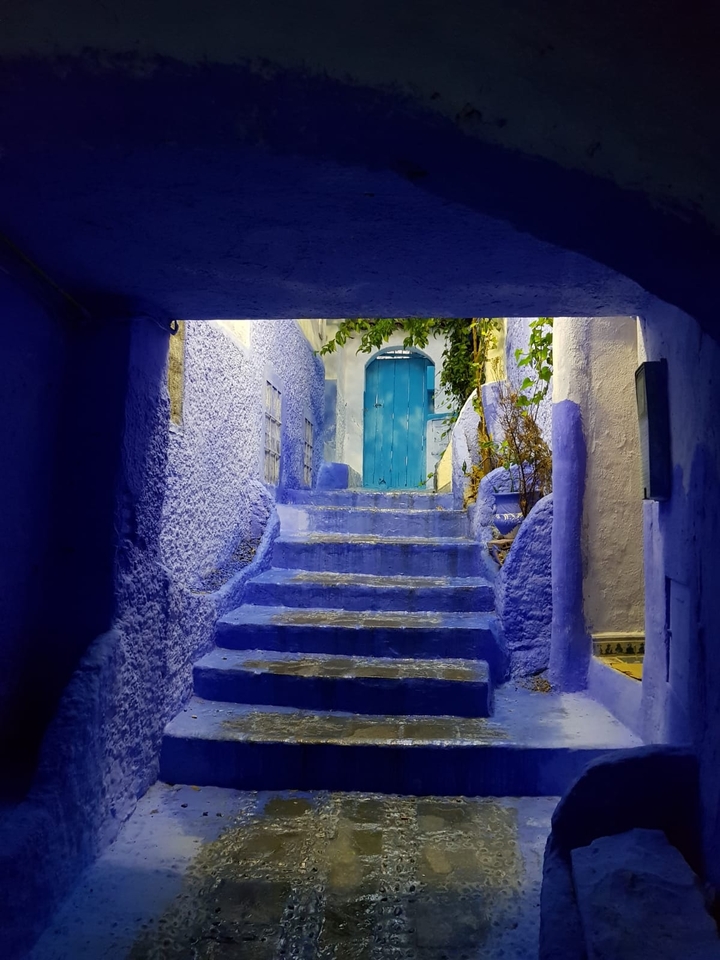 Blue-painted alleyway with steps and a blue door, typical Moroccan architecture