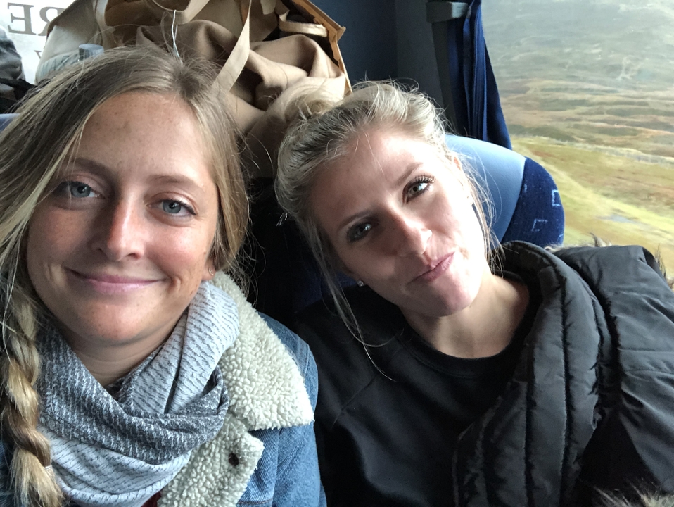 Deux femmes souriantes dans un autocar avec des vues panoramiques par la fenêtre.