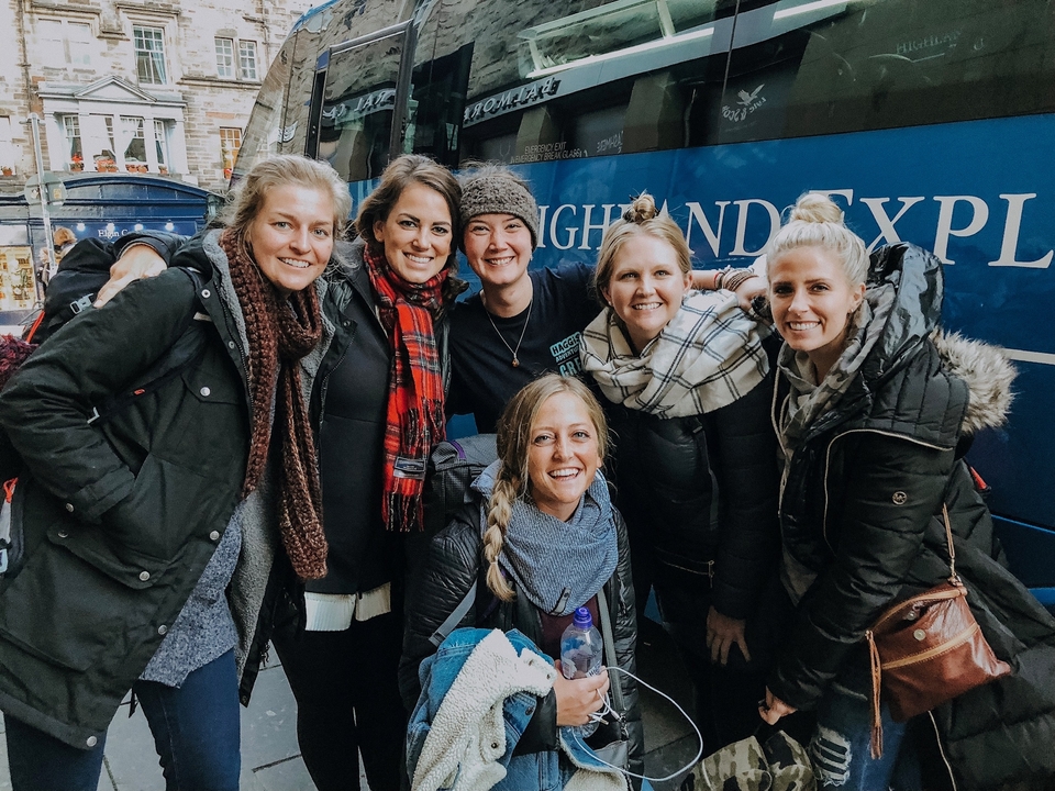 Groupe de femmes souriantes devant un autocar de tourisme bleu avec les mots « Highland Explorer ».