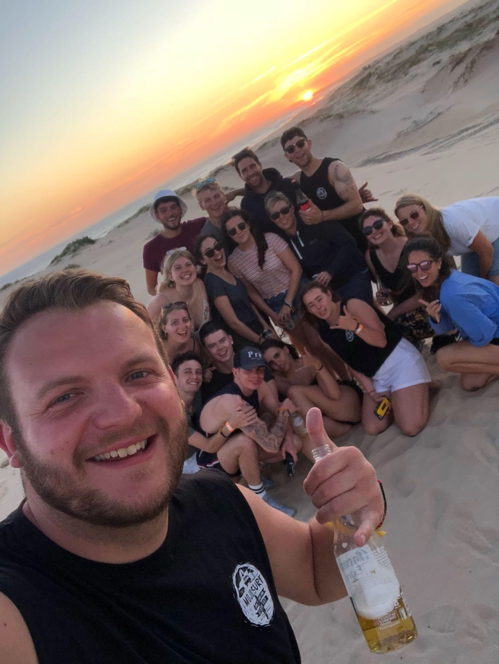 Large group of people smiling on a sandy beach.