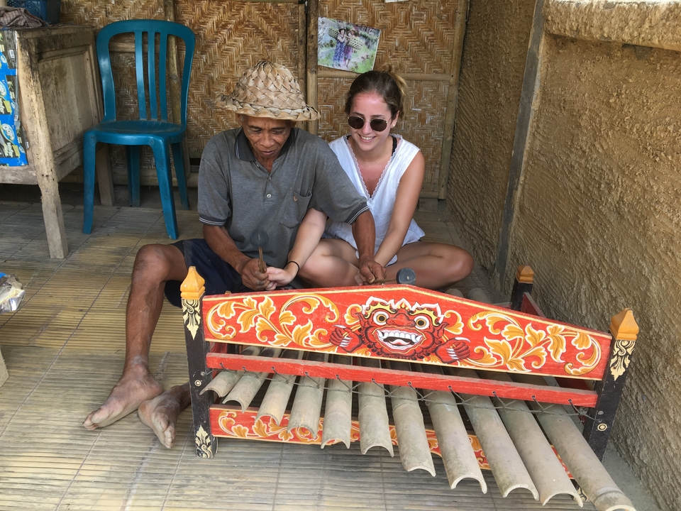 Elderly man teaching a woman to play a traditional wooden xylophone.