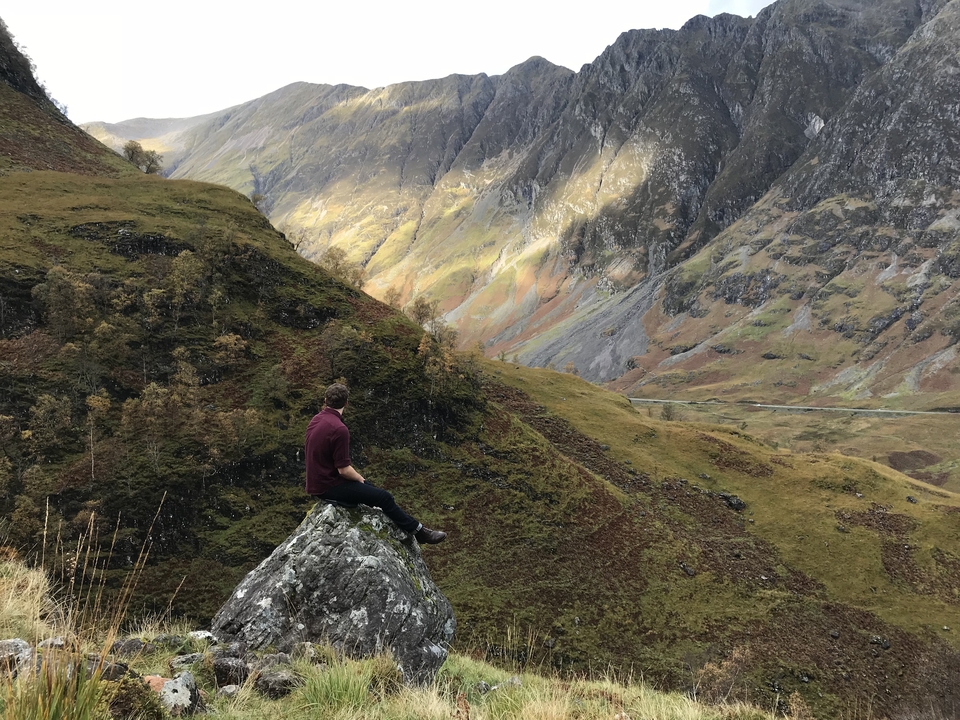 Man sitting on a rock enjoying the view of a scenic mountain landscape.