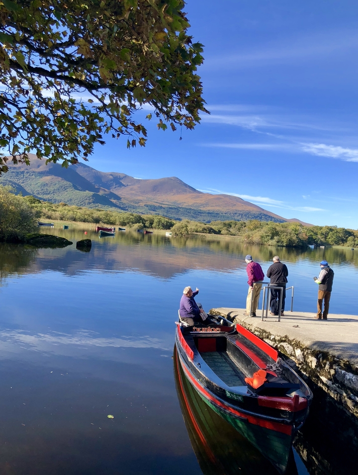 People fishing and boating on a lake with mountains in the background.