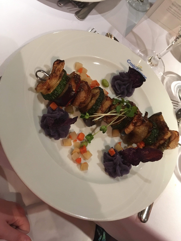 Brochette de légumes avec purée violette et légumes en dés dans une assiette.