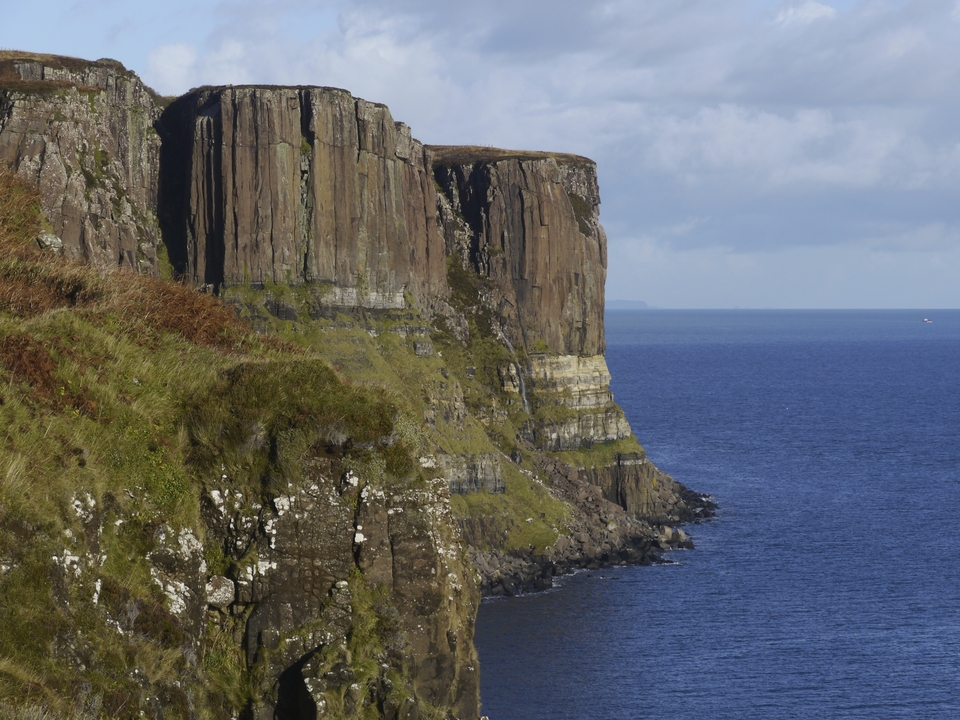 Dramatic cliffs meeting the sea under a blue sky.
