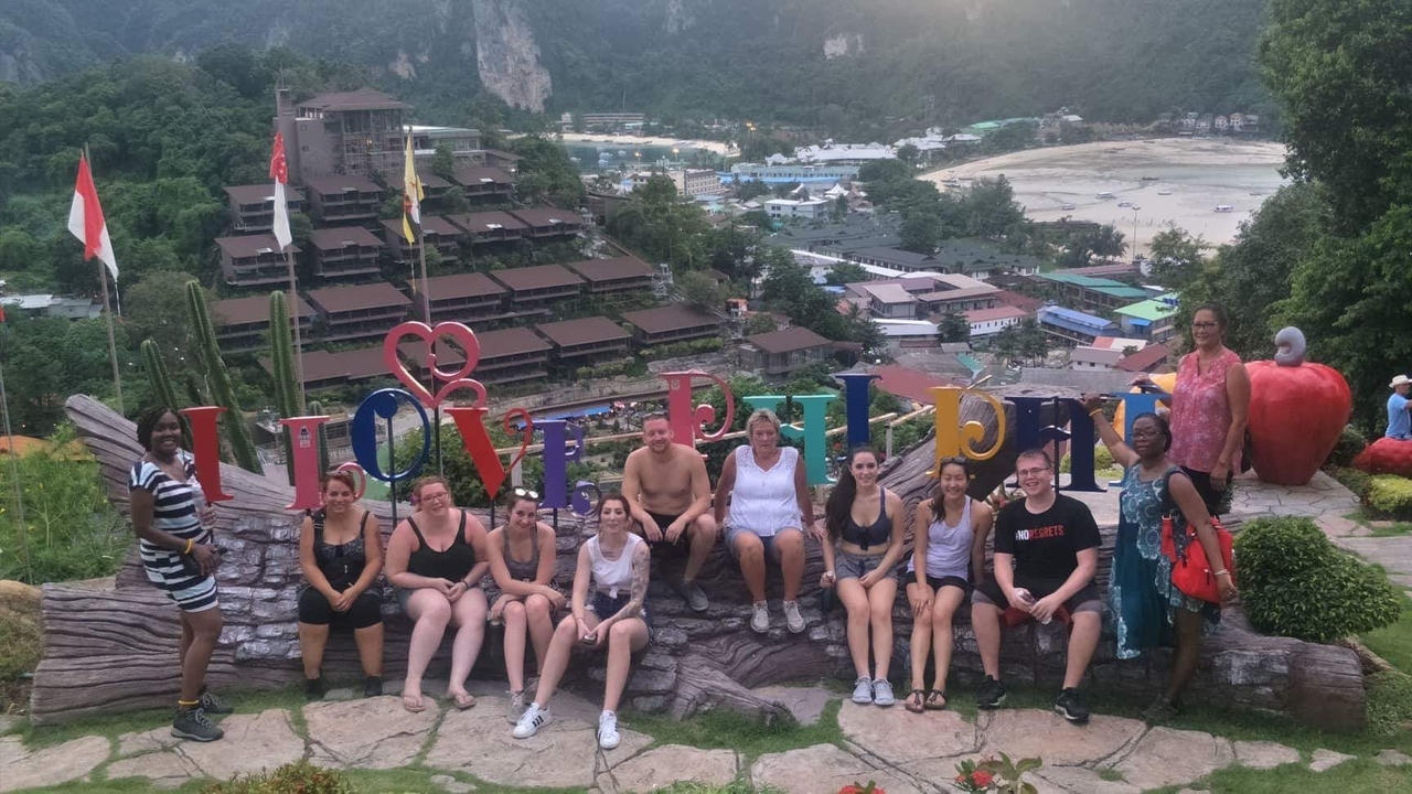 Group of tourists sitting in front of a sign with mountains in the background.