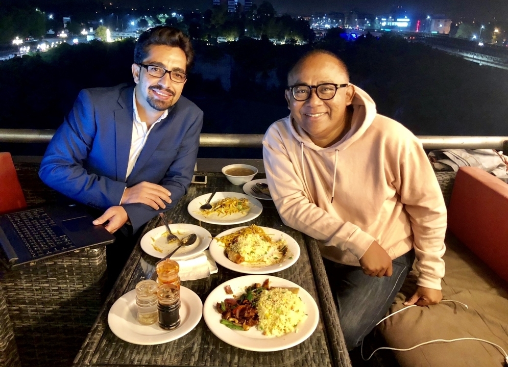 Two men dining at a table with multiple dishes at night.