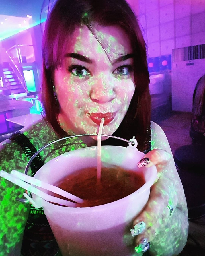 Person drinking from a bowl with colorful lighting in a club.
