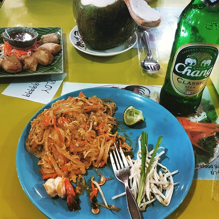 Plate of pad thai with a Chang beer bottle on a table.