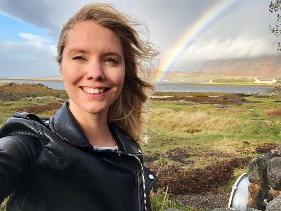 Person taking a selfie with a rainbow in the background over a field.