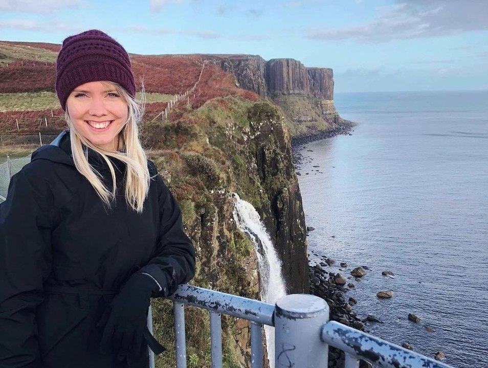 Person posing in front of a cliff and waterfall.
