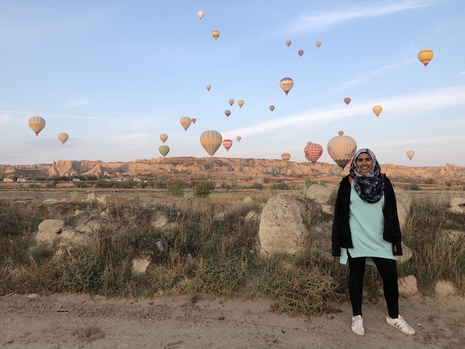 Person posing in front of hot air balloons.