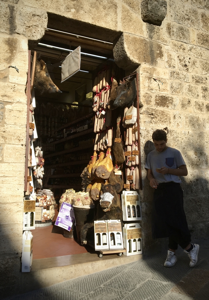Un homme debout devant une boutique avec des viandes suspendues.