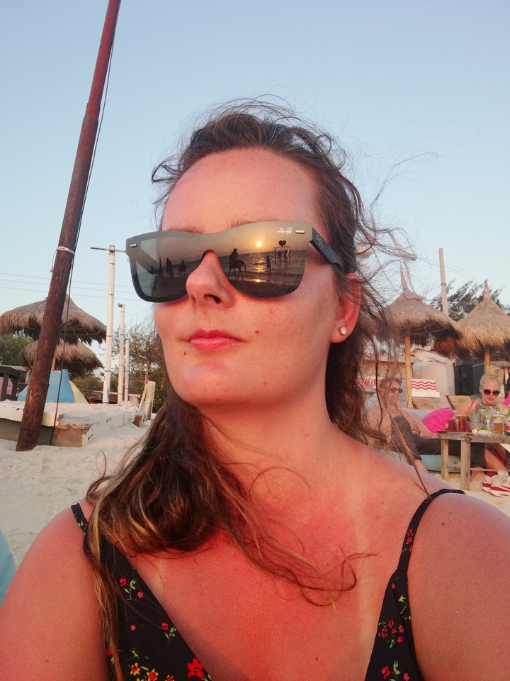 Close-up of a person wearing sunglasses reflecting a beach scene.