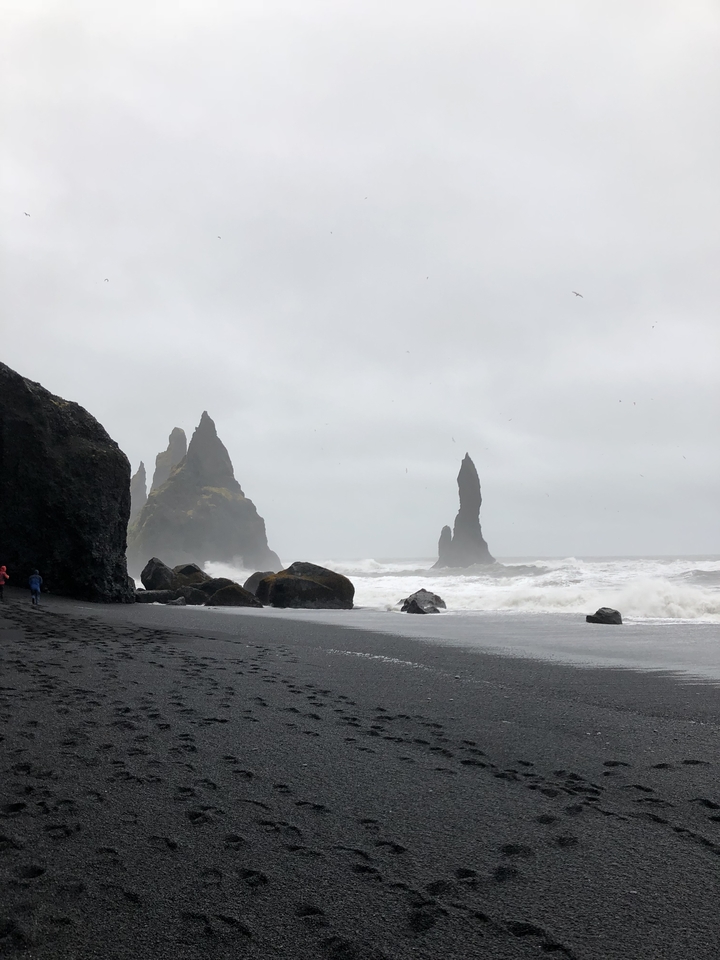 Jagged rock formations on a black sand beach.
