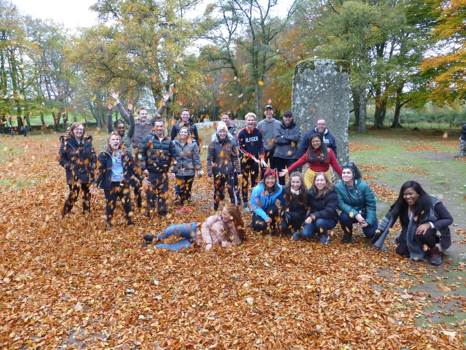 A group of people playing with leaves in a park during autumn.