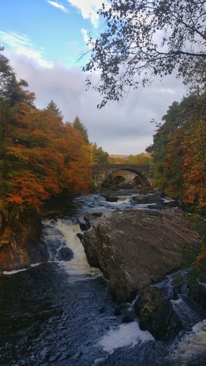 Stone bridge over a rushing river surrounded by autumn trees.