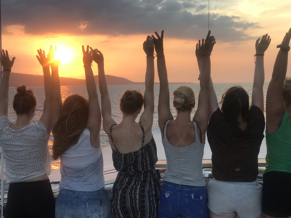 Group of people with raised hands watching a sunset from a boat.