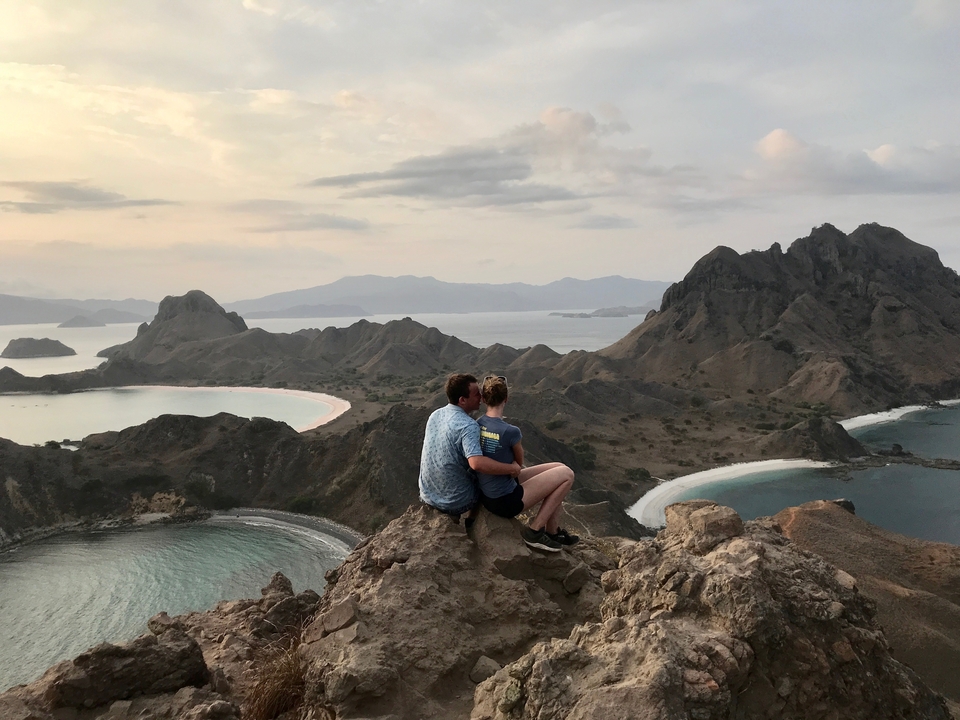 Couple sitting on rocks overlooking the sea and hills.