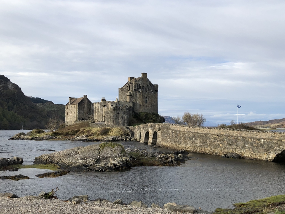 Castle on a small island with a bridge and Scottish flag.