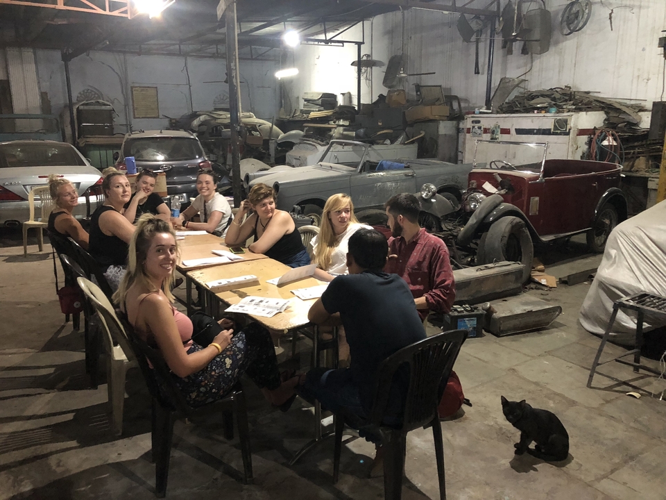 Groupe de personnes ayant une réunion dans un atelier avec des voitures anciennes.