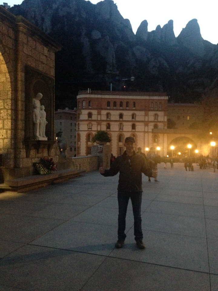 Person posing in front of historic buildings at night.