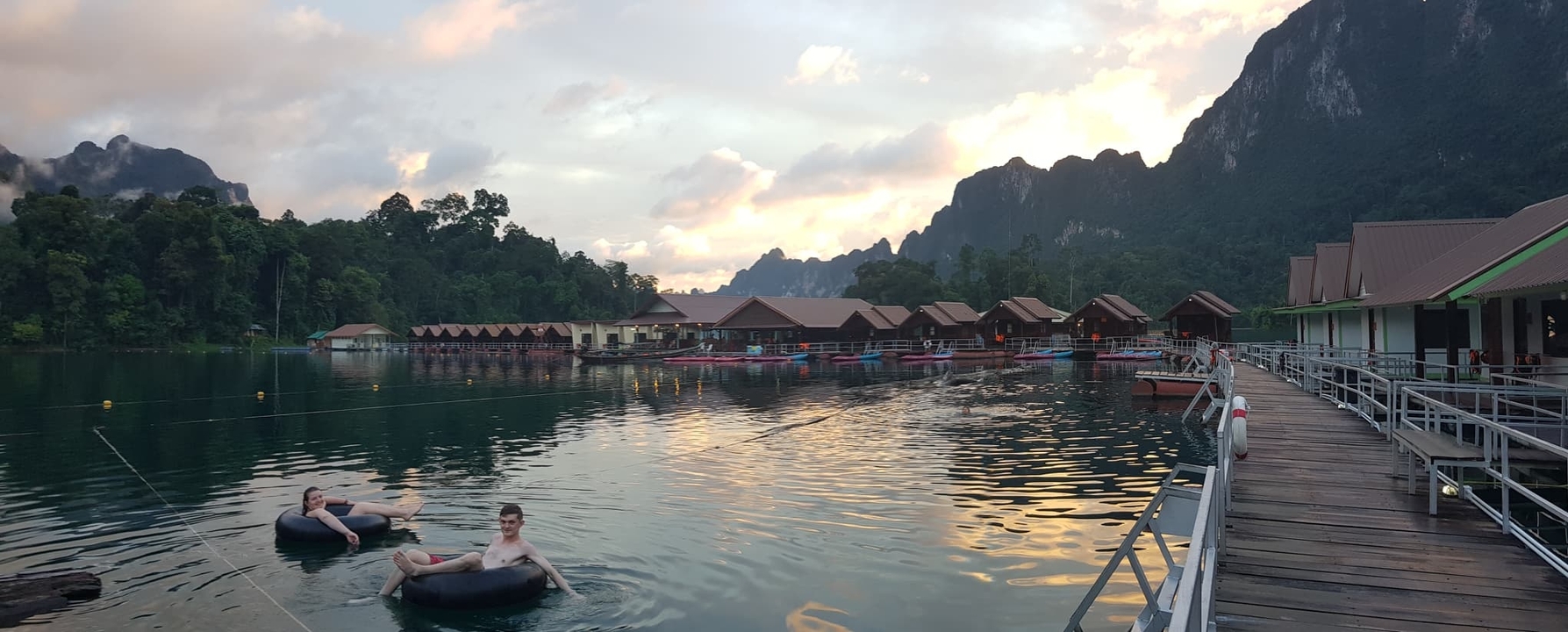 People enjoying a lake with floating bungalows at sunset.